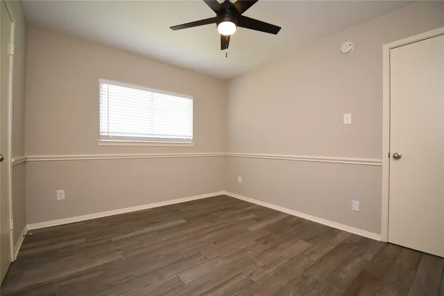 an empty room with wooden floor fan and windows