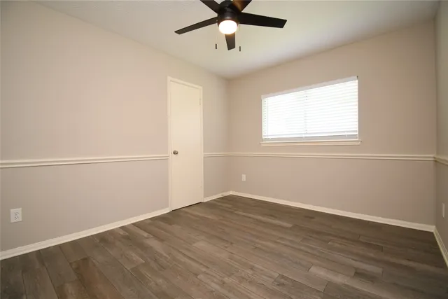 an empty room with wooden floor fan and windows