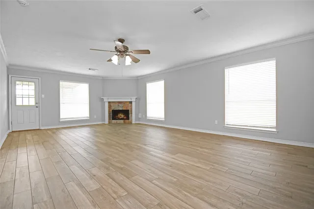 an empty room with wooden floor ceiling fan and windows