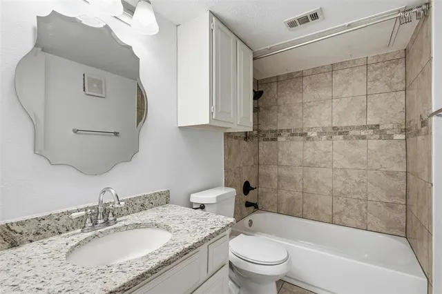 a bathroom with a granite countertop bathtub shower sink vanity and toilet