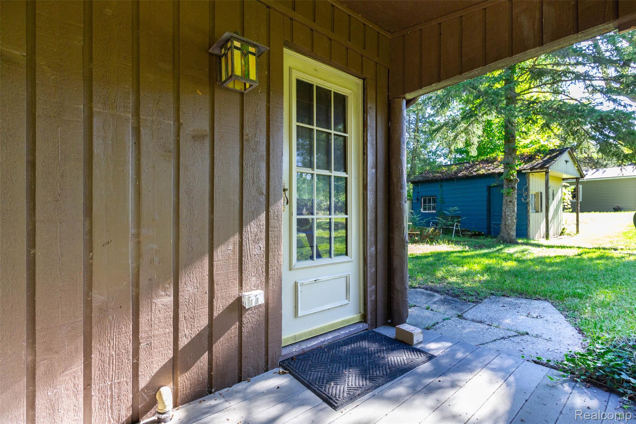 14044 Ridgemont Drive Gregory, MI 48137 - Photo 5 of 33 Board and batten siding, outdoor wall lantern, glass panel door, concrete porch, and established trees
