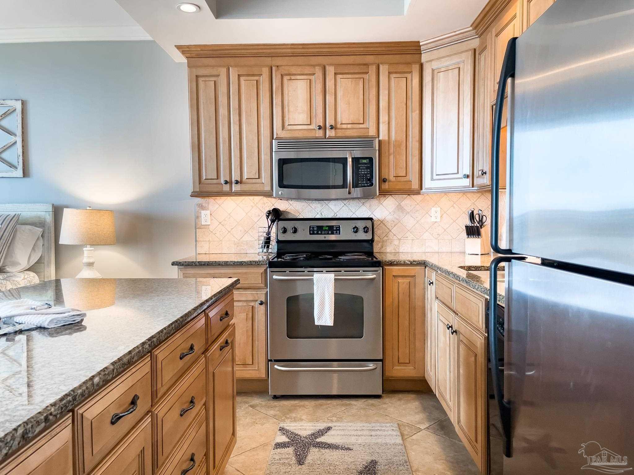 16287 Perdido Key Drive, Unit 104 Pensacola, FL 32507 - Photo 12 of 32 a kitchen with granite countertop a sink a stove top oven and cabinetry