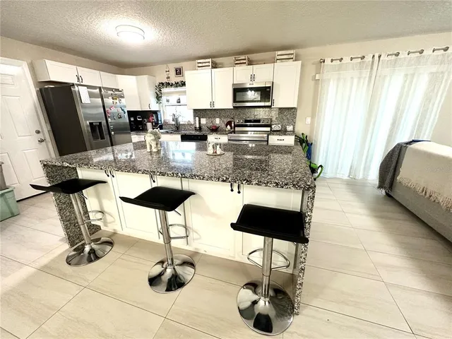 a kitchen with stainless steel appliances kitchen island granite countertop a table chairs and a refrigerator