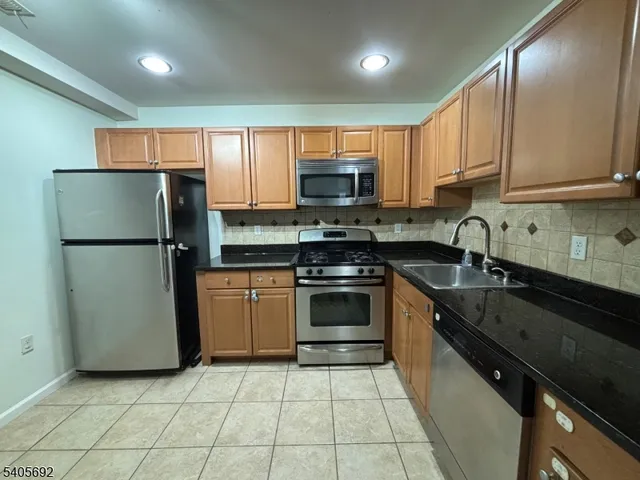 a kitchen with granite countertop a refrigerator a sink a stove top oven and cabinets