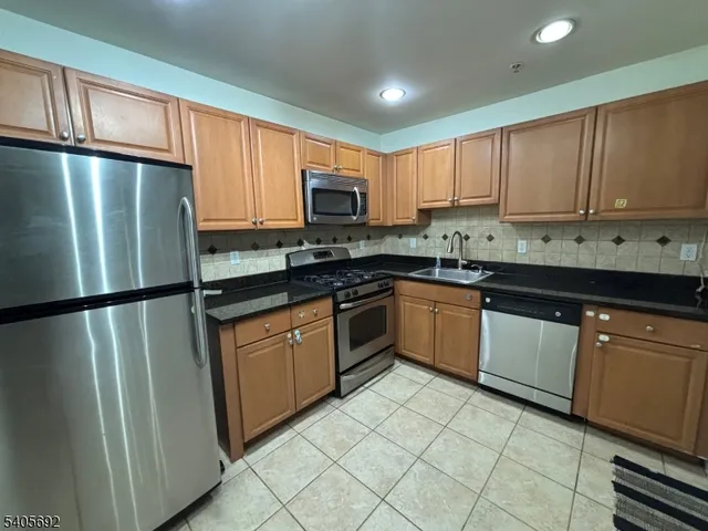 a kitchen with granite countertop a refrigerator a sink a stove top oven and cabinets