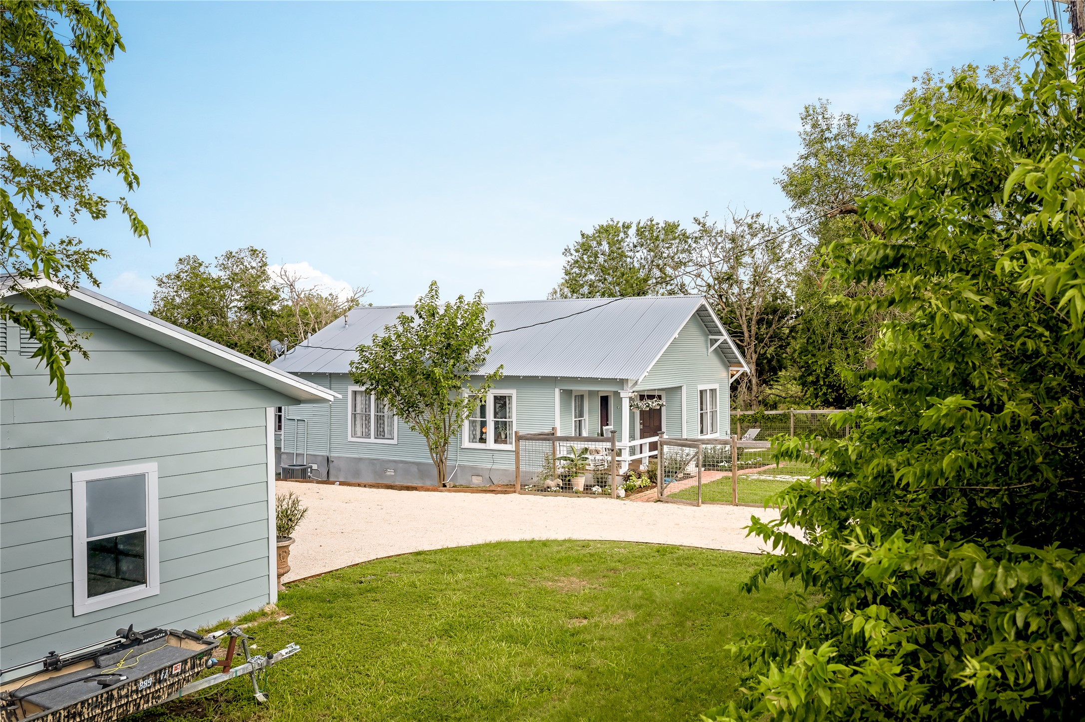 372 Old Lockhart Road Lockhart, TX 78644 - Photo 35 of 40 A graceful home with a metal roof, front porch, and gravel driveway, surrounded by mature greenery.