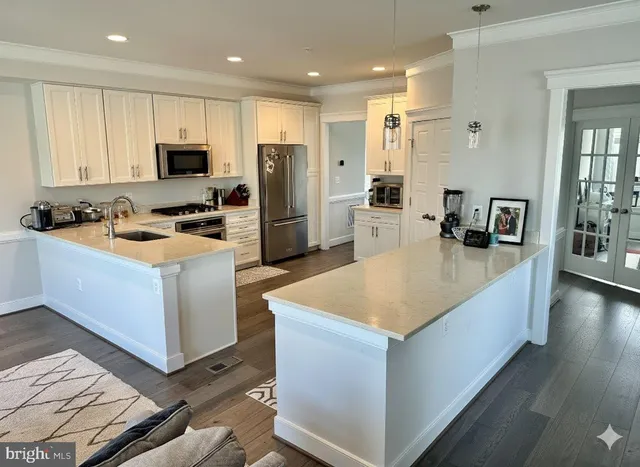 a kitchen with stainless steel appliances granite countertop a white stove top oven a sink dishwasher a refrigerator and white cabinets with wooden floor
