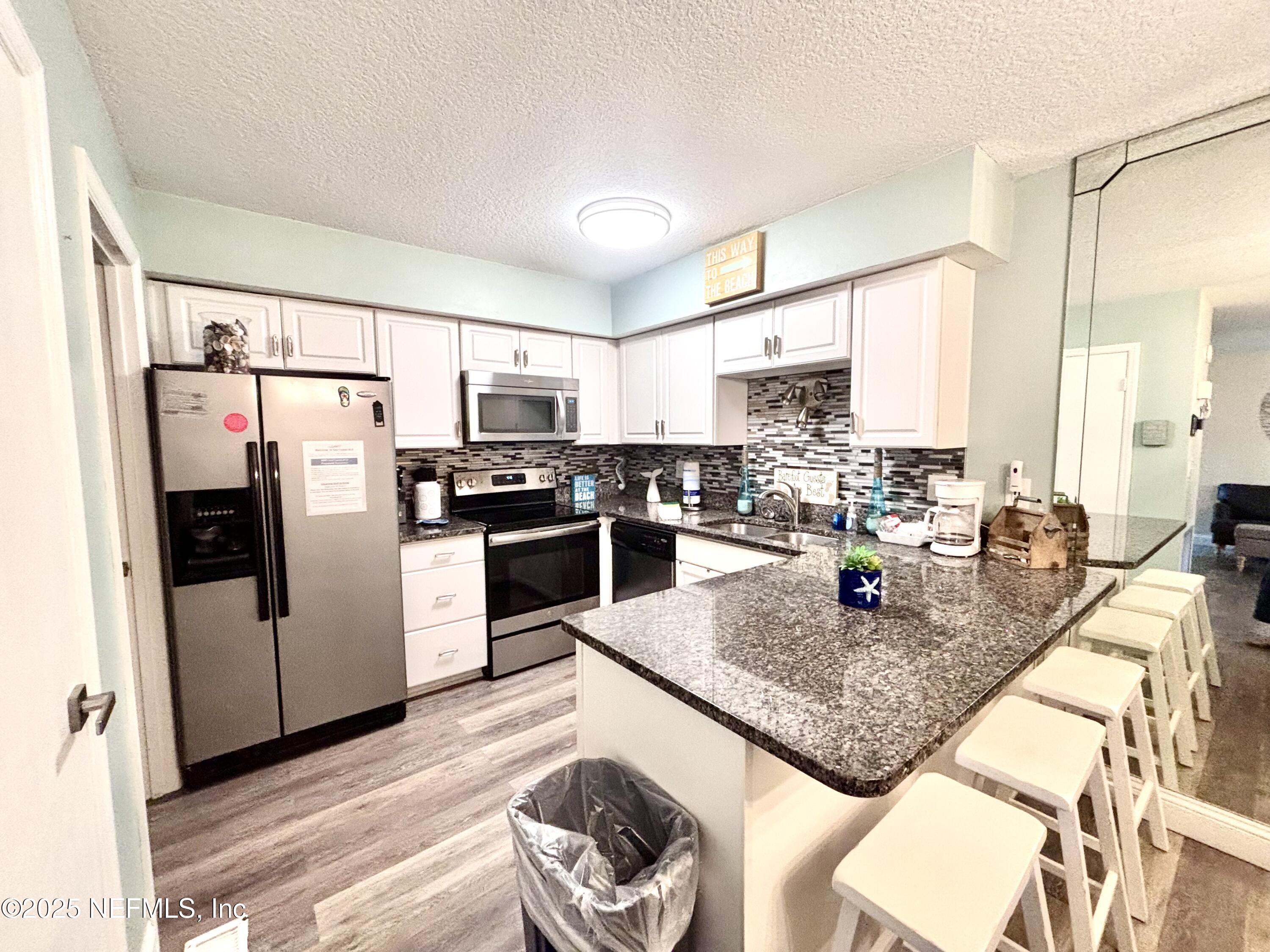 3165 1st Avenue, Unit 13 Fernandina Beach, FL 32034 - Photo 13 of 37 a kitchen with stainless steel appliances granite countertop a refrigerator a stove a sink a dining table and chairs