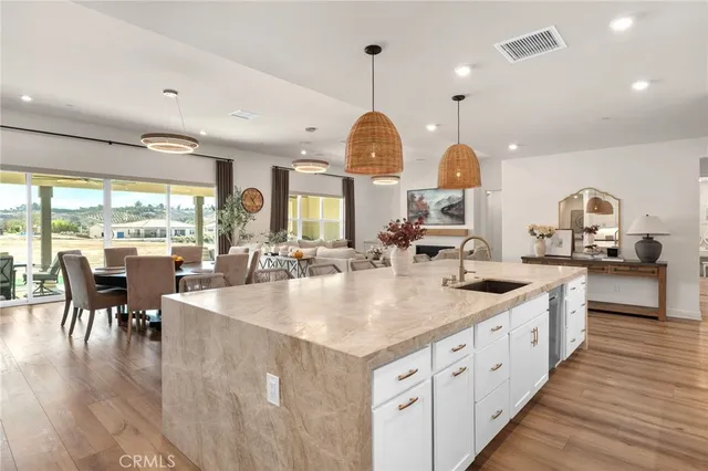 a large kitchen with kitchen island a large center island a sink a stove and a dining table with wooden floor