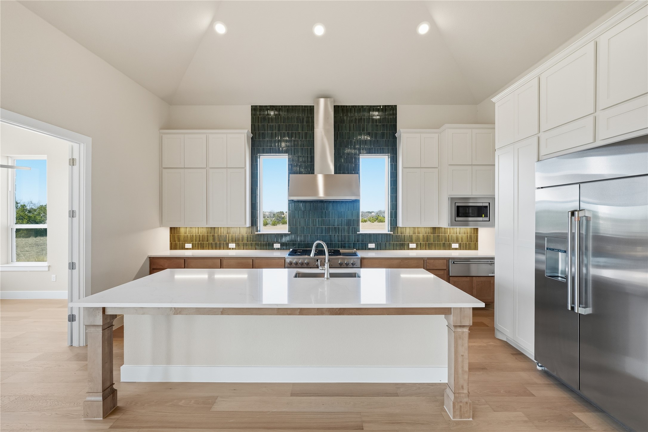 1209 Doelling Drive Georgetown, TX 78633 - Photo 7 of 31 Kitchen featuring tasteful backsplash, built in appliances, a kitchen island with sink, lofted ceiling, and light wood-style flooring