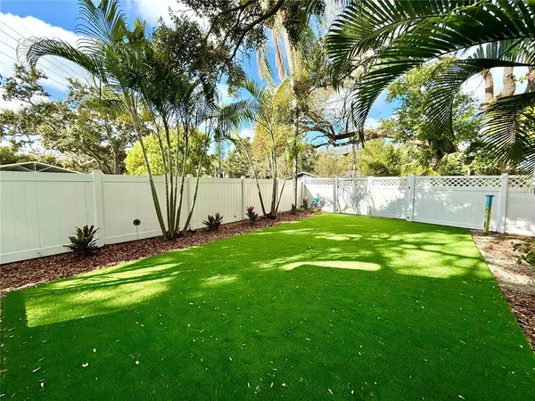 a view of a backyard with table and chairs potted plants and large tree