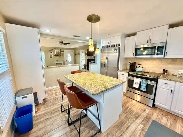 a kitchen with stainless steel appliances granite countertop a refrigerator a stove a sink dishwasher and a dining table with wooden floor