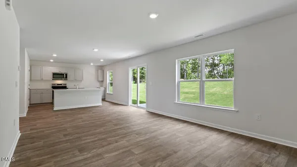 a view of an empty room with kitchen and window
