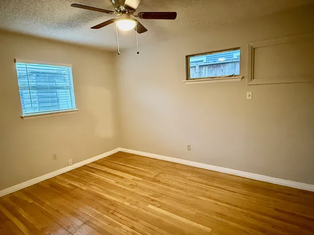a view of an empty room with wooden floor and a ceiling fan