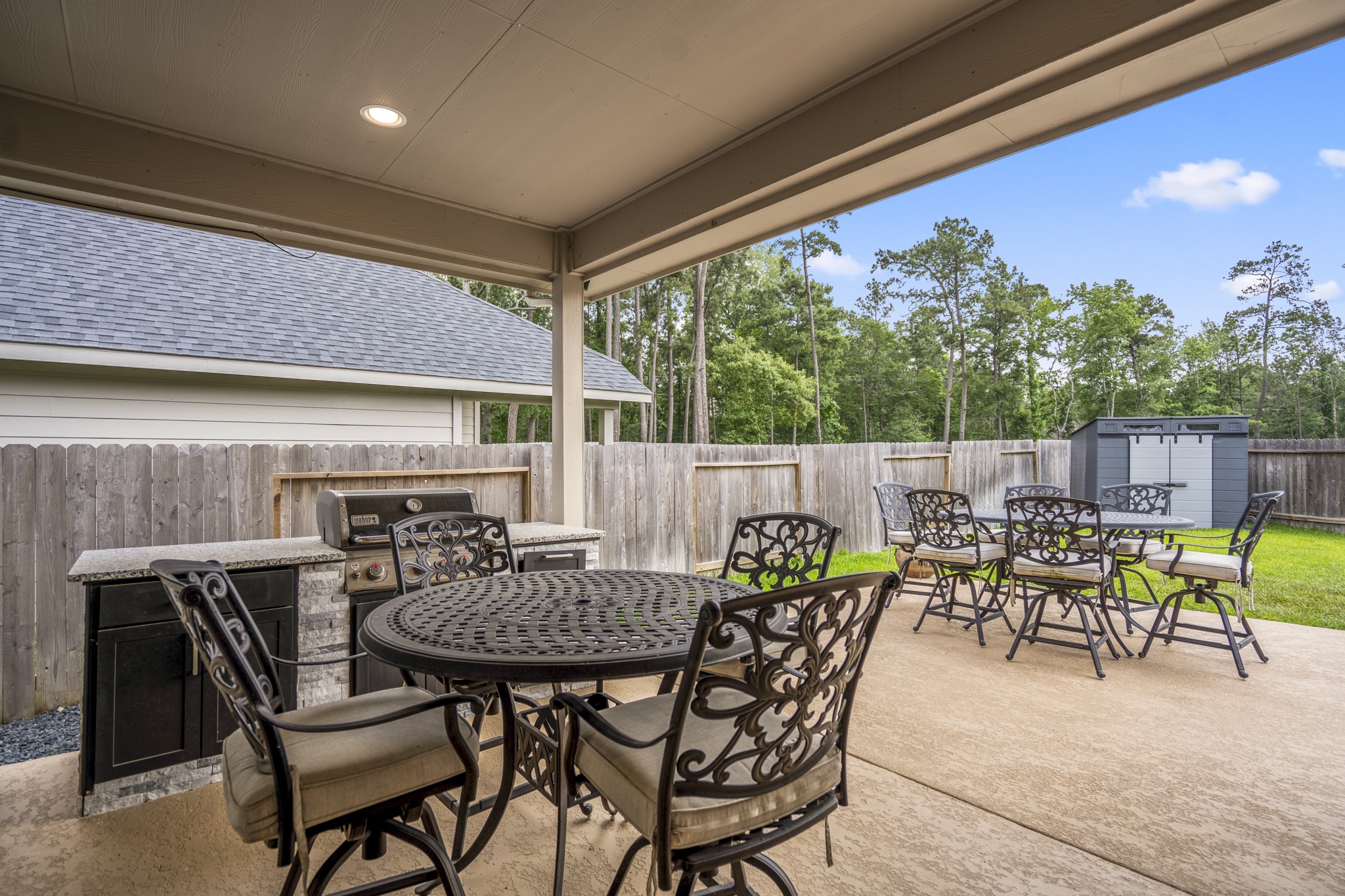 304 Mullins Court Montgomery, TX 77316 - Photo 30 of 50 The photo features a spacious covered patio with a built-in grill and overlooks a fenced backyard with a storage shed, offering privacy and a lush tree-lined view.