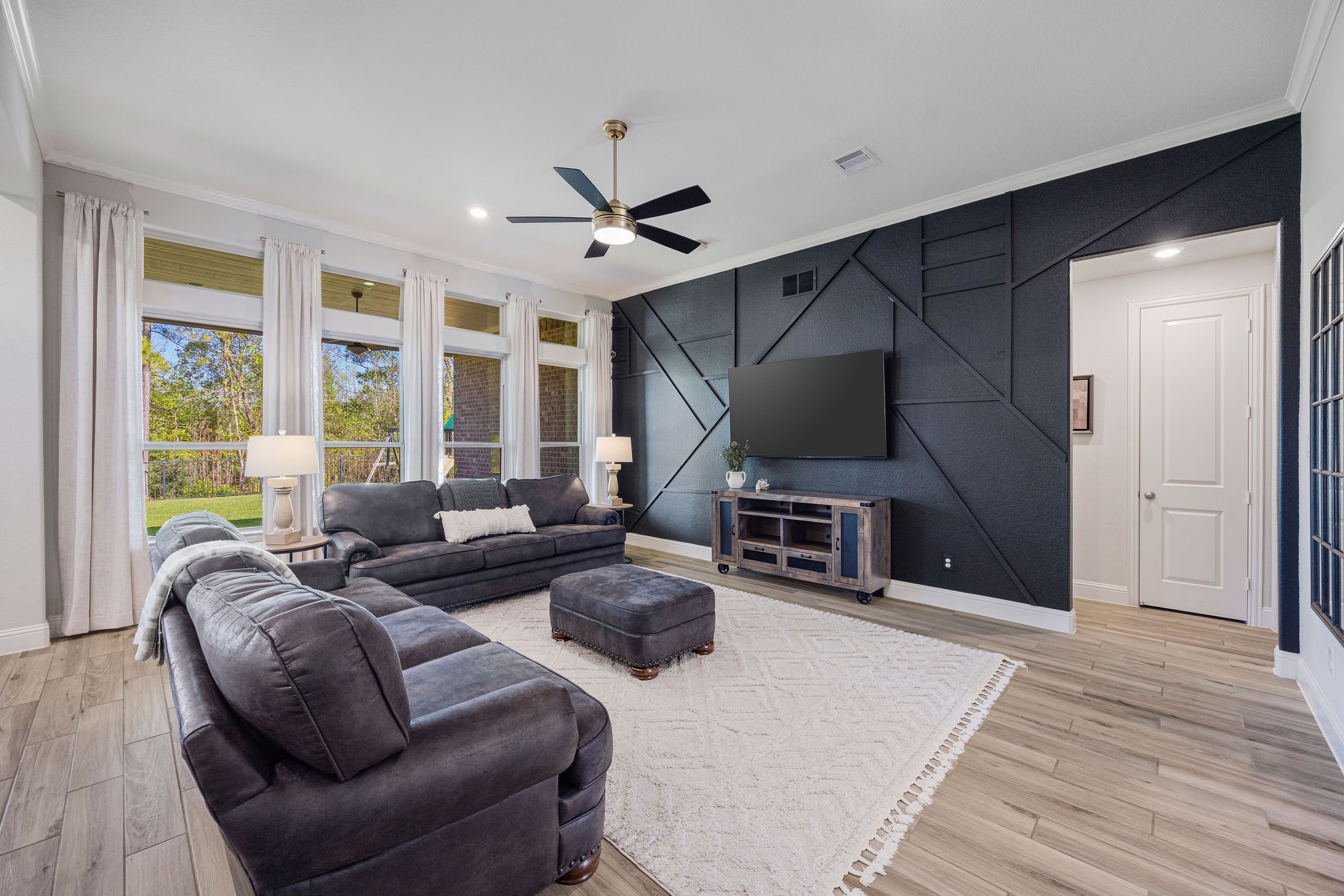 13103 Six Rivers Drive Humble, TX 77346 - Photo 10 of 44 A light-filled living room with high ceilings, continuous wood-look tile, and a striking accent wall, offering standout views of the wooded backyard.