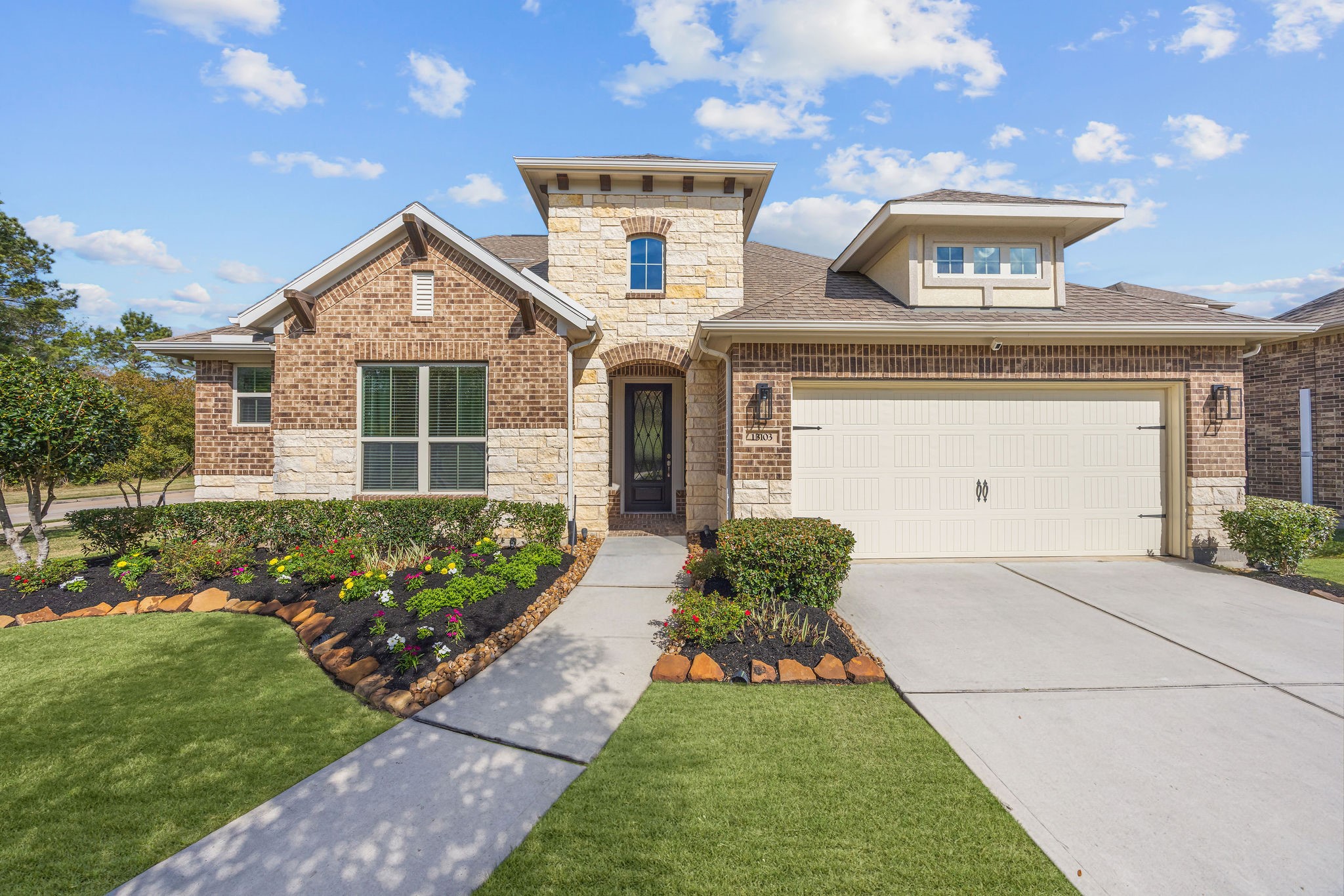 Striking elevation featuring a blend of brick, stone, and stucco exterior complemented by fresh landscaping, and modern light fixtures.