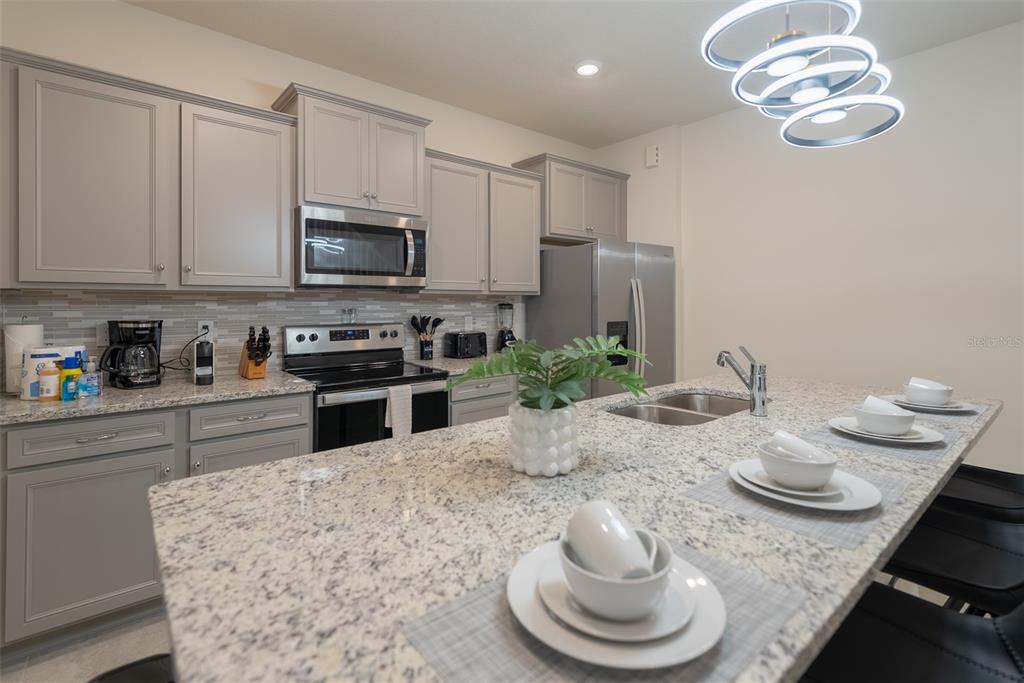 4470 Kaipo Road Davenport, FL 33897 - Photo 8 of 34 a kitchen with stainless steel appliances granite countertop a sink a stove a microwave a refrigerator cabinets and living room view