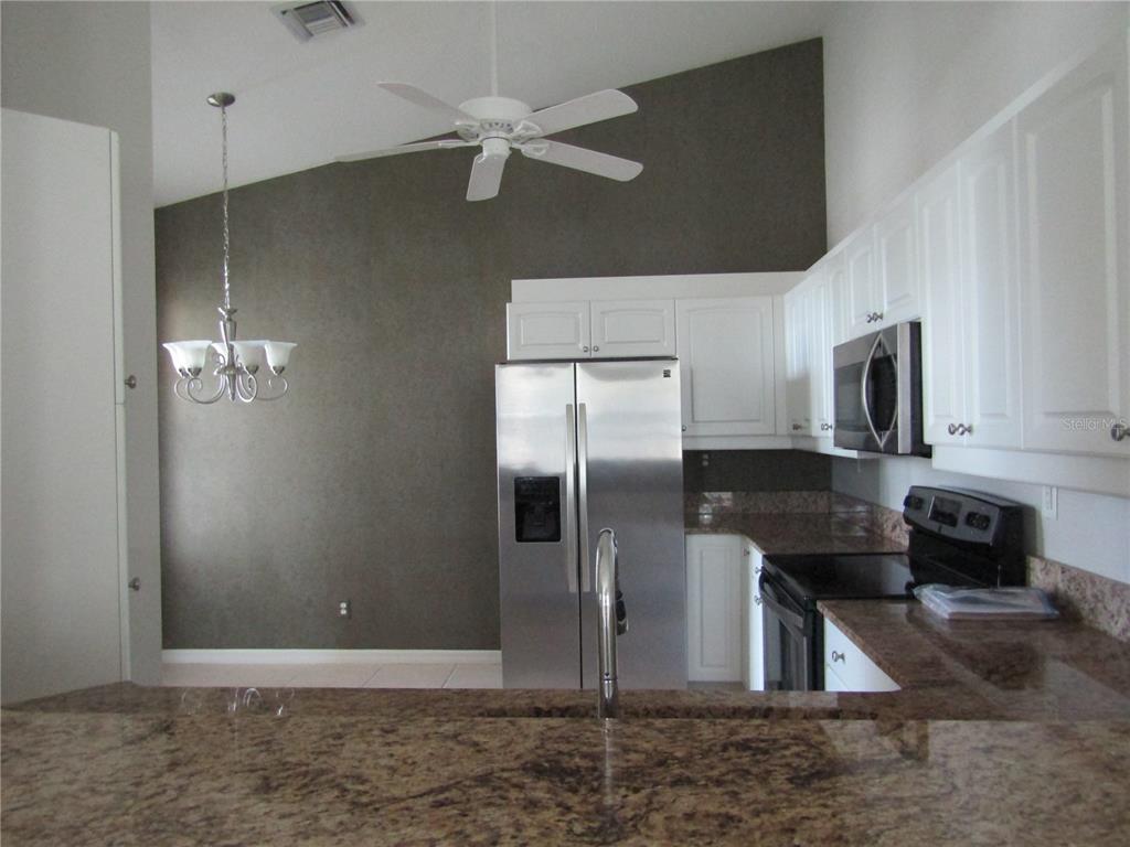 1669 Monarch Drive, Unit 204 Venice, FL 34293 - Photo 5 of 17 a kitchen with stainless steel appliances kitchen island granite countertop a refrigerator a stove and a sink with wooden floor