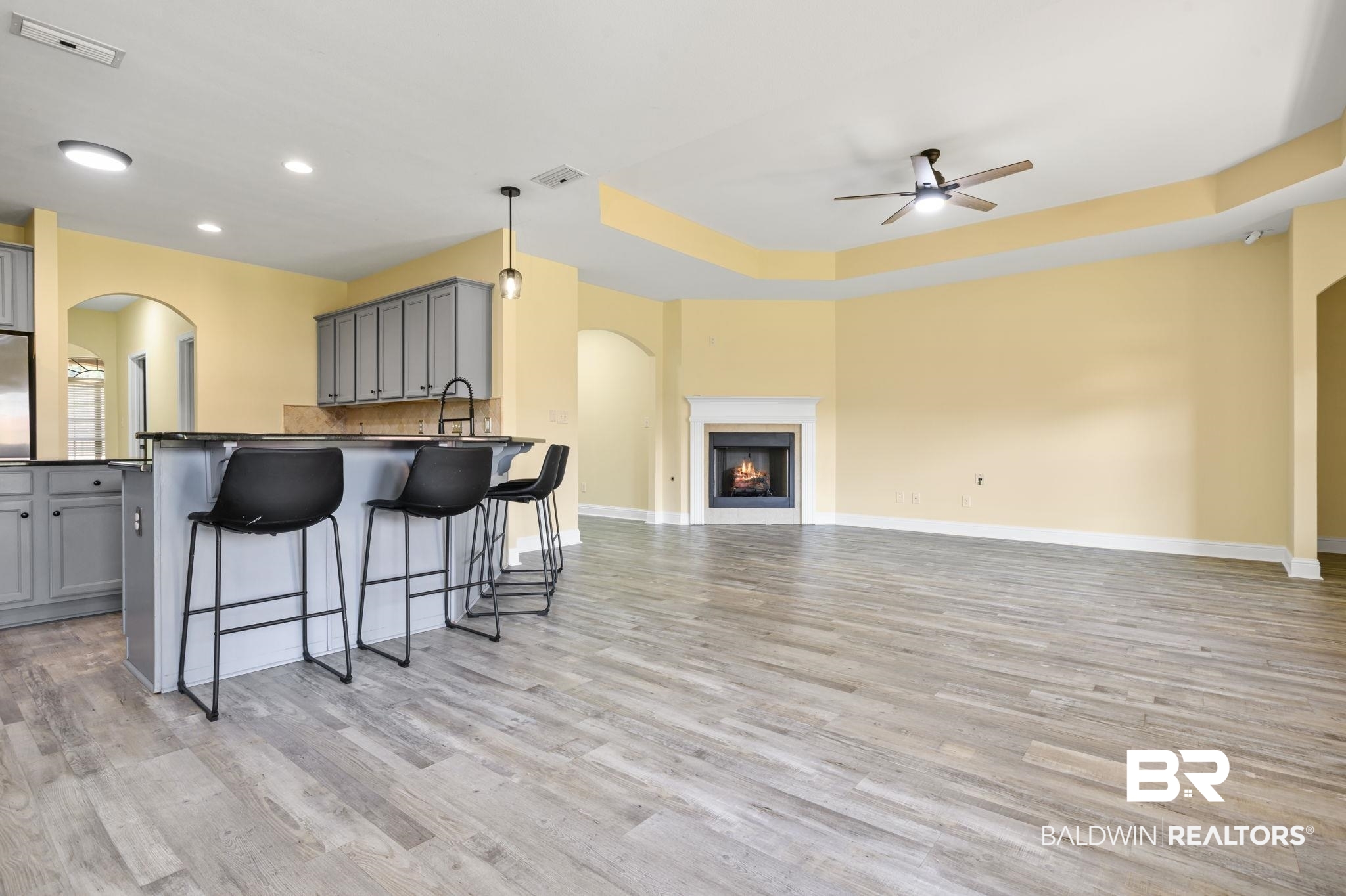 25234 Fairfax Road Daphne, AL 36526 - Photo 19 of 45 Kitchen featuring arched walkways, gray cabinets, dark countertops, a kitchen breakfast bar, and a warm lit fireplace