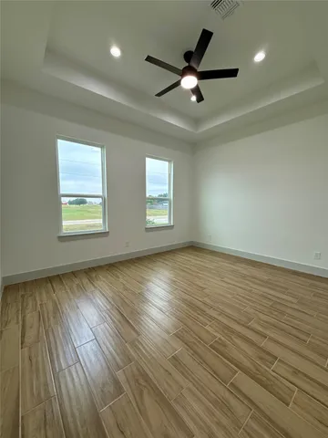 an empty room with wooden floor fan and windows