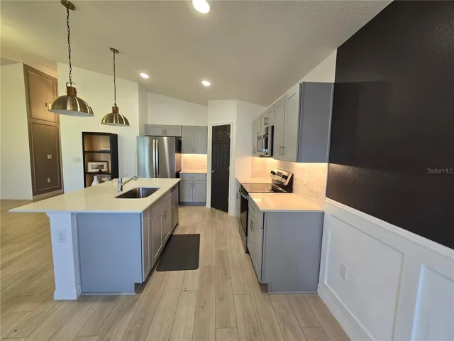 a large kitchen with stainless steel appliances a large counter top and wooden floor