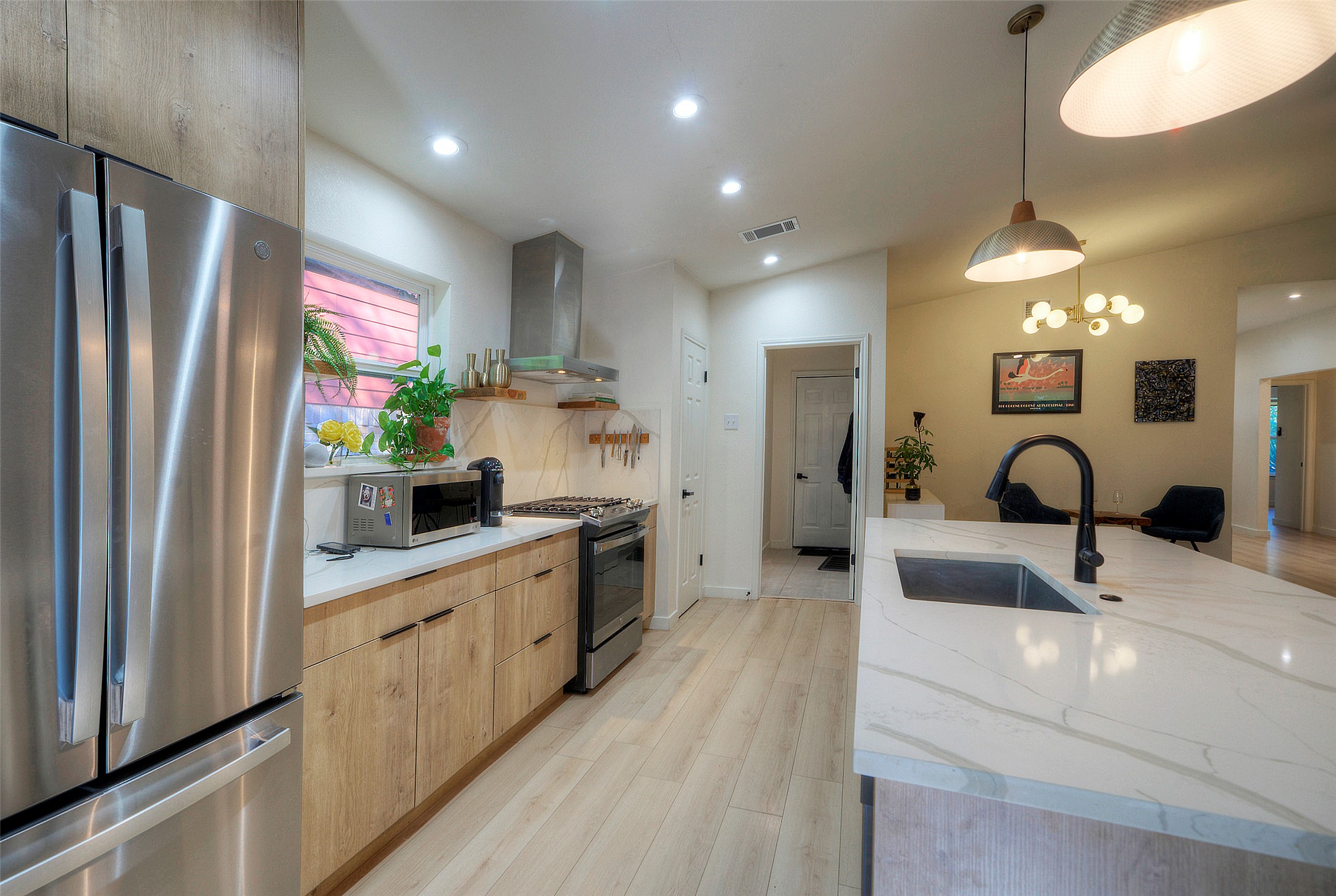 8406 Los Ranchos Drive Austin, TX 78749 - Photo 7 of 32 A contemporary kitchen showcasing light wood cabinetry and sleek stainless steel appliances, highlighted by recessed and pendant lighting.