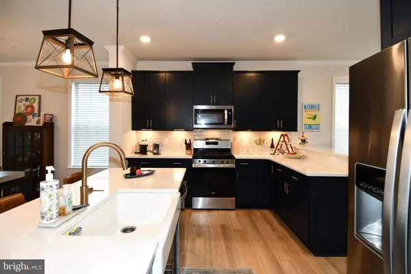 a kitchen with stainless steel appliances a sink dishwasher a refrigerator a microwave oven with white cabinets and wooden floor