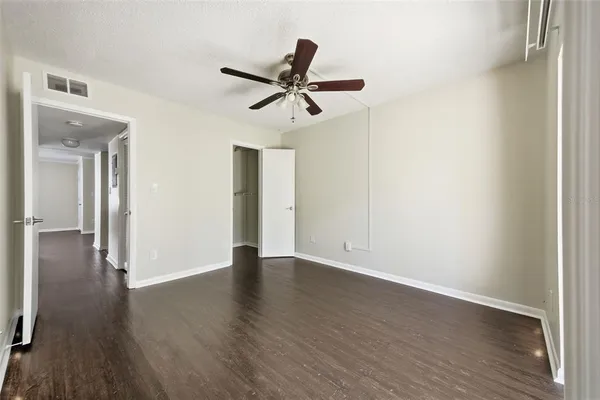a view of an empty room with wooden floor and a ceiling fan