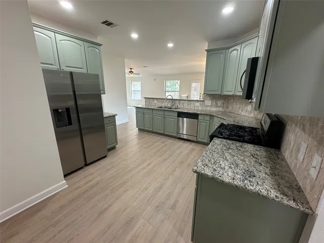 a kitchen with stainless steel appliances granite countertop a refrigerator a sink dishwasher a stove and white countertops with wooden floor