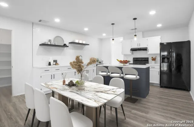 a kitchen with stainless steel appliances granite countertop a dining table chairs refrigerator and cabinets