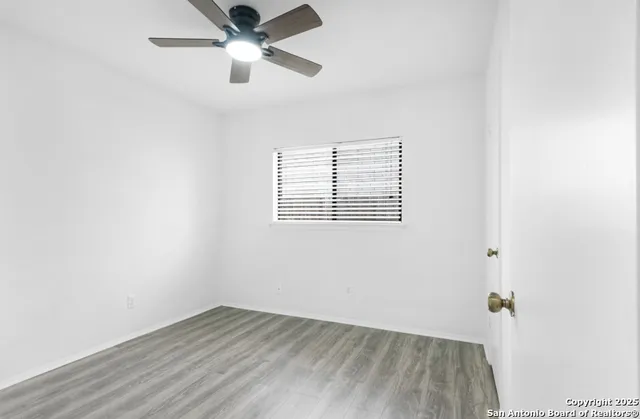 an empty room with wooden floor ceiling fan and windows