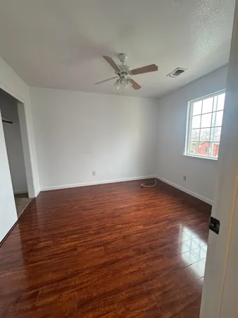 an empty room with wooden floor fan and windows