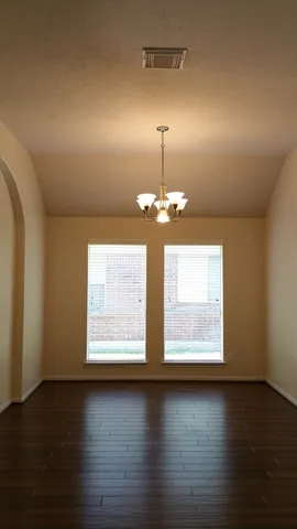 an empty room with wooden floor chandelier and windows