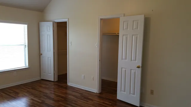an empty room with wooden floor closet and windows