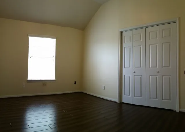 an empty room with wooden floor and windows with curtains