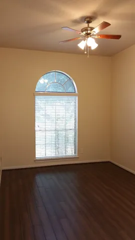 an empty room with wooden floor fan and windows