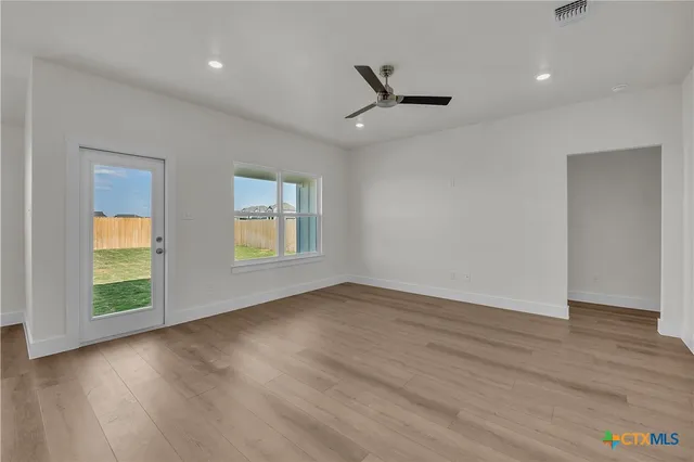 an empty room with wooden floor a ceiling fan and windows