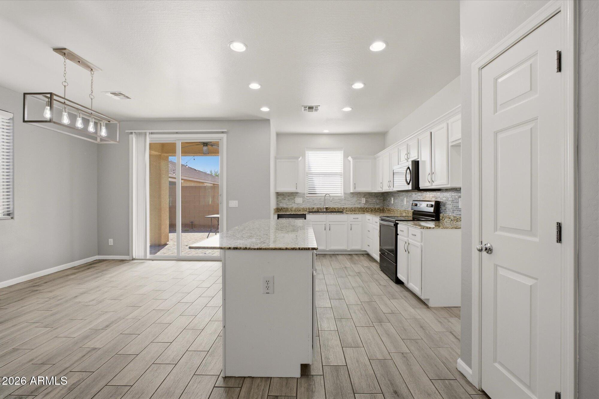 3347 East Roland Street Mesa, AZ 85213 - Photo 11 of 25 a kitchen with stainless steel appliances granite countertop a refrigerator a sink dishwasher a stove and white cabinets with wooden floor