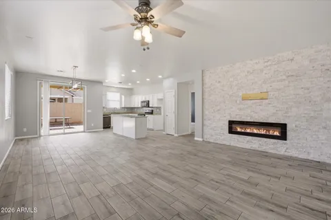 an empty room with wooden floor kitchen view and a ceiling fan