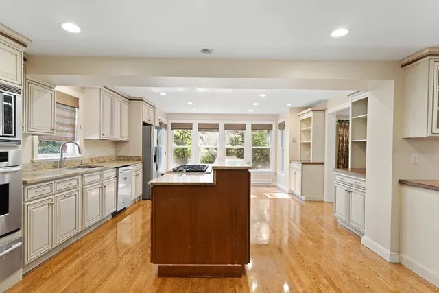 a large kitchen with stainless steel appliances granite countertop a refrigerator a stove top oven a sink dishwasher and white cabinets with wooden floor