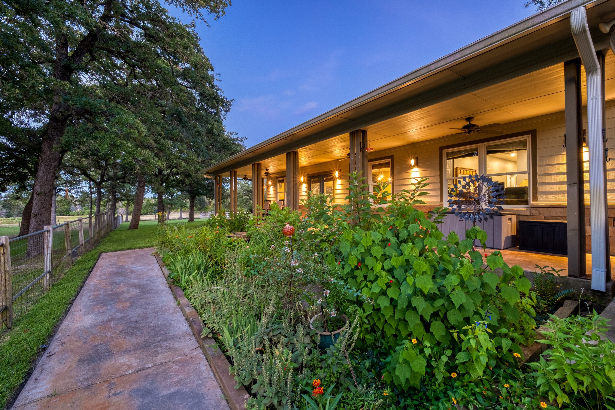 1474 County Rd B Lexington, TX 78947 - Photo 28 of 34 A welcoming front porch, adorned with lush garden beds, extends along a charming pathway leading to the property's entrance.