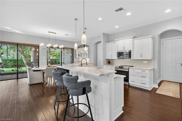 a kitchen with stainless steel appliances granite countertop a stove a refrigerator a kitchen island a stove and white cabinets with wooden floor