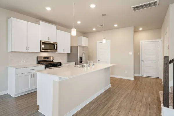 a kitchen with stainless steel appliances granite countertop a refrigerator a sink a stove and white cabinets with wooden floor