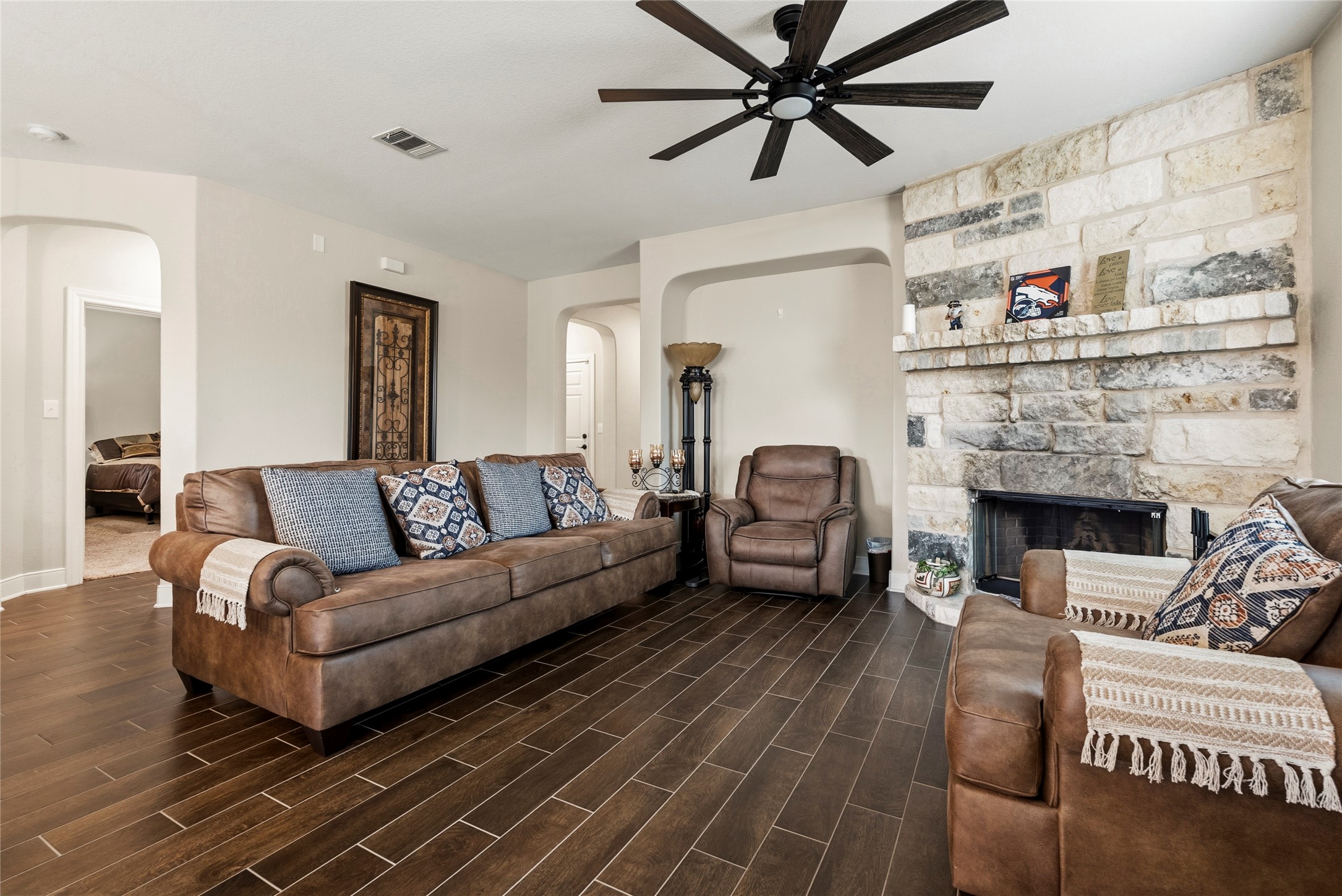 105 West Point Way Elgin, TX 78621 - Photo 21 of 27 Spacious living area featuring a stone fireplace with hearth, wood-finish flooring, and a ceiling fan with dark blades