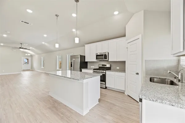 a kitchen with stainless steel appliances kitchen island a sink a stove a refrigerator and white cabinets with wooden floor