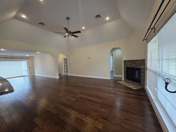 an empty room with wooden floor a ceiling fan a fireplace and windows