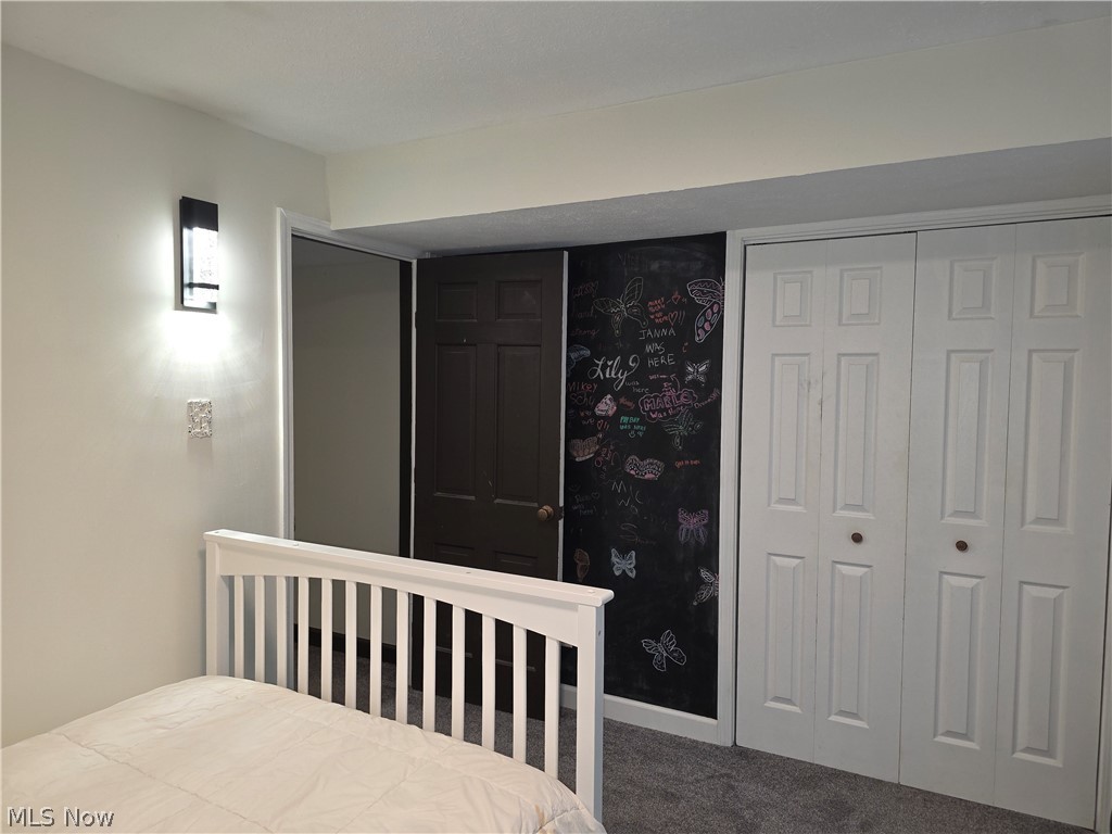 2868 Shade Road Akron, OH 44333 - Photo 32 of 49 Wall-mounted sconce lighting illuminates the room, featuring a dark paneled door, a chalkboard wall, and white bi-fold closet doors, all set against neutral painted walls and gray carpet