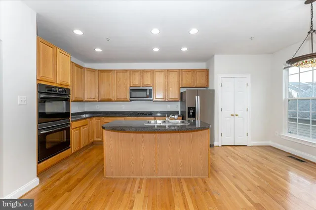a kitchen with stainless steel appliances granite countertop a stove a sink and a refrigerator with wooden floors