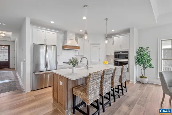 a kitchen with stainless steel appliances kitchen island granite countertop a refrigerator a stove a sink a dining table and chairs with wooden floor